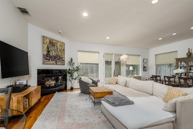 living area featuring a glass covered fireplace, visible vents, recessed lighting, and wood finished floors