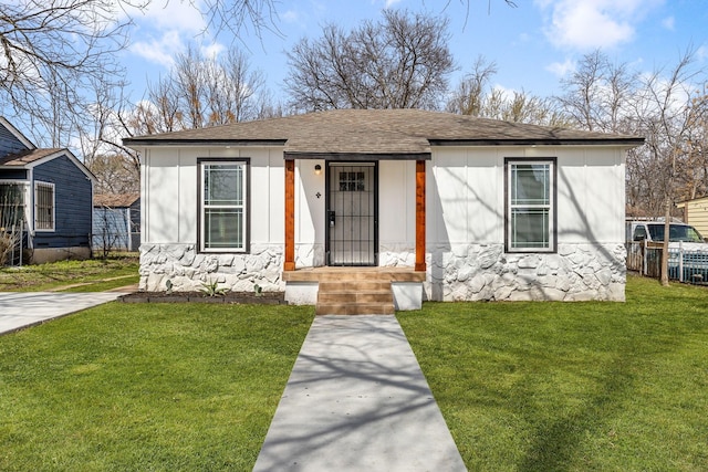 bungalow-style home featuring stone siding, a shingled roof, fence, and a front lawn