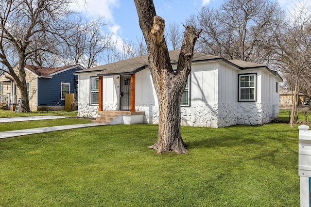 view of front of house with stone siding, a shingled roof, a front lawn, and board and batten siding