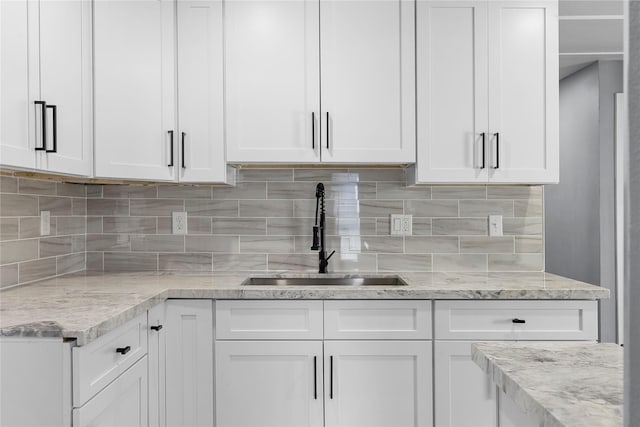 kitchen featuring light stone countertops, backsplash, white cabinets, and a sink