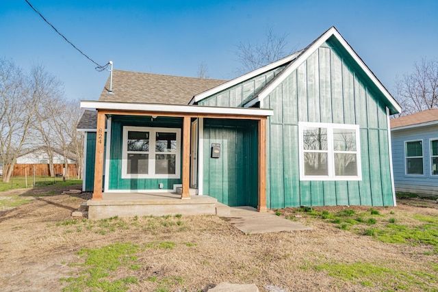 view of front of home with covered porch, a shingled roof, fence, and board and batten siding