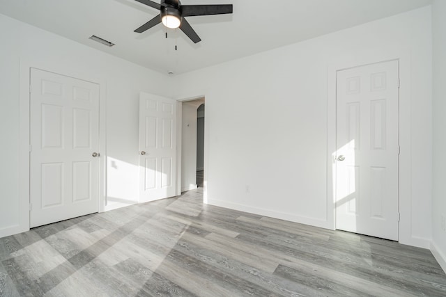 unfurnished bedroom featuring baseboards, visible vents, a ceiling fan, arched walkways, and wood finished floors