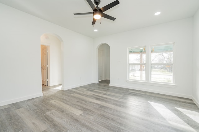 empty room featuring arched walkways, recessed lighting, light wood-style flooring, and baseboards