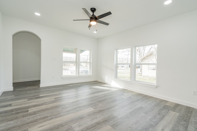 empty room with baseboards, arched walkways, a ceiling fan, wood finished floors, and recessed lighting