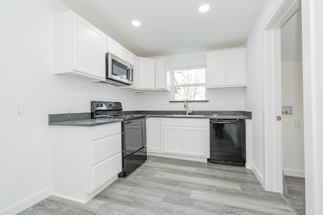 kitchen with dark countertops, black appliances, white cabinets, and a sink