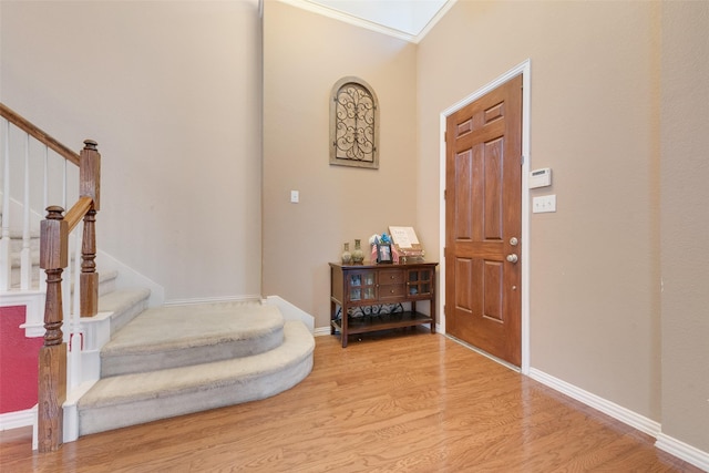 foyer entrance with a skylight, baseboards, stairway, crown molding, and light wood-type flooring