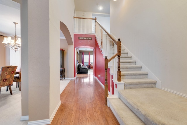 entrance foyer with baseboards, arched walkways, wood finished floors, stairs, and a chandelier