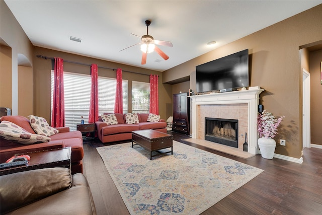 living room featuring visible vents, dark wood-type flooring, a ceiling fan, a tile fireplace, and baseboards