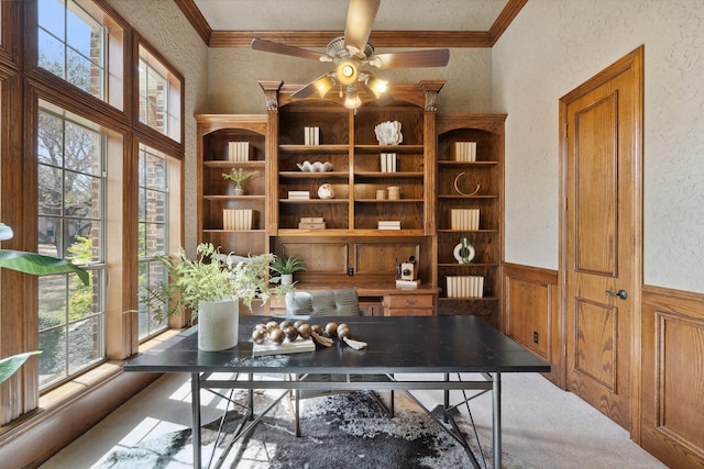 office space with a ceiling fan, ornamental molding, wainscoting, and a textured wall