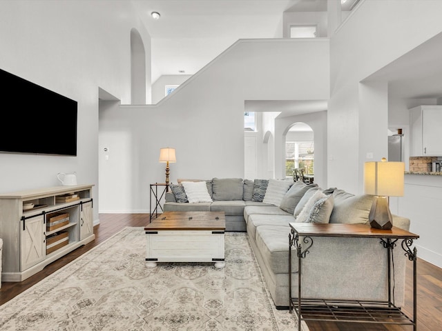 living room featuring baseboards, arched walkways, high vaulted ceiling, and wood finished floors