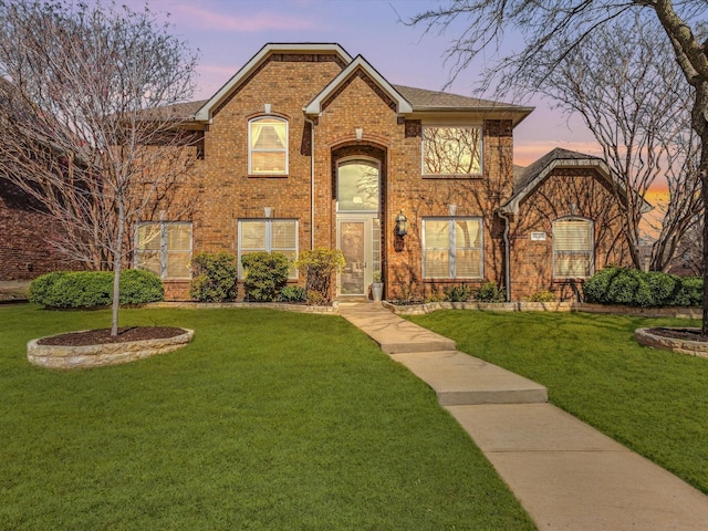 traditional home featuring a lawn, brick siding, and roof with shingles