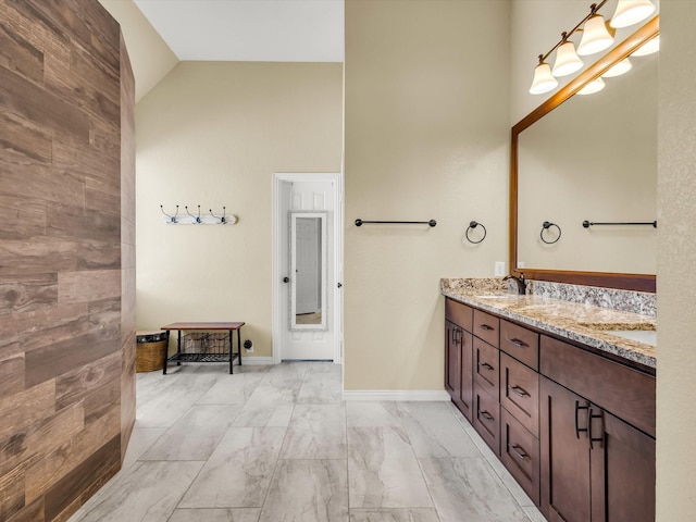 full bathroom with baseboards, lofted ceiling, double vanity, marble finish floor, and a sink