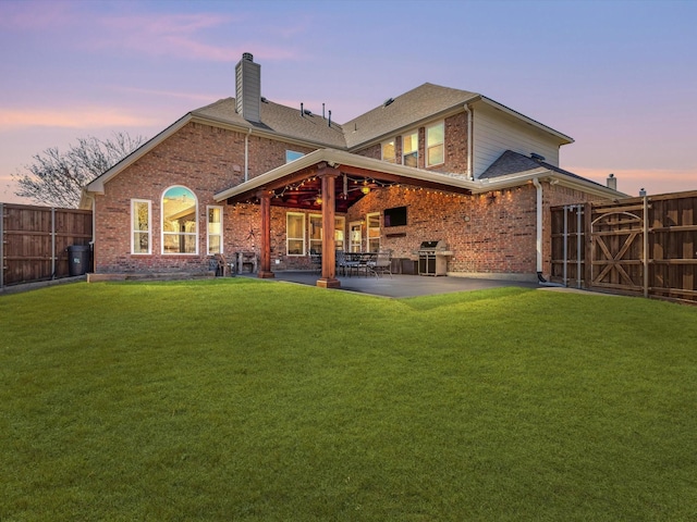 back of property at dusk featuring a yard, fence, brick siding, and a patio area