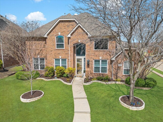 view of front of house with a front lawn, brick siding, and roof with shingles