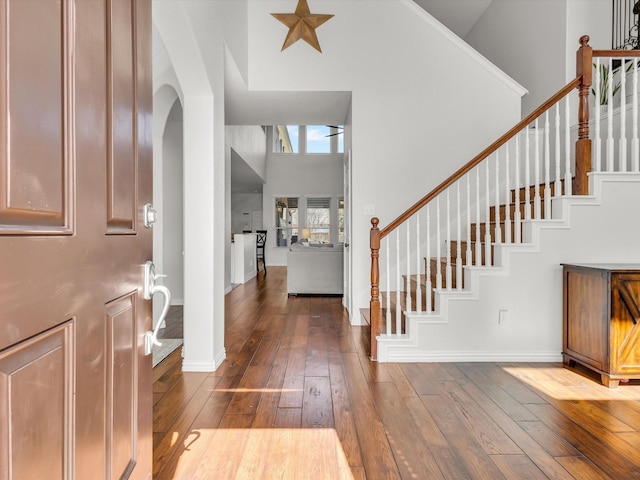 foyer entrance featuring stairway, baseboards, arched walkways, dark wood-type flooring, and a towering ceiling