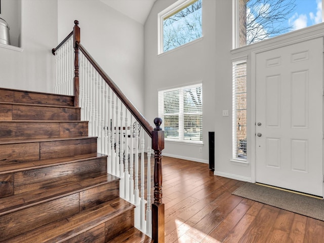 foyer featuring stairs, baseboards, wood-type flooring, and high vaulted ceiling