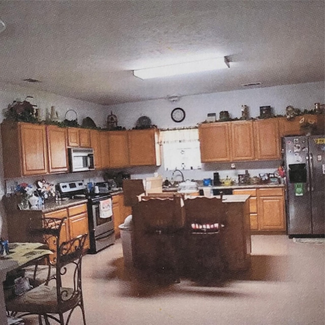 kitchen with a textured ceiling, black fridge with ice dispenser, stainless steel electric range, a center island, and brown cabinetry