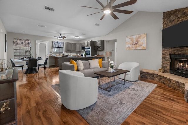 living room featuring visible vents, a ceiling fan, lofted ceiling, wood finished floors, and a fireplace