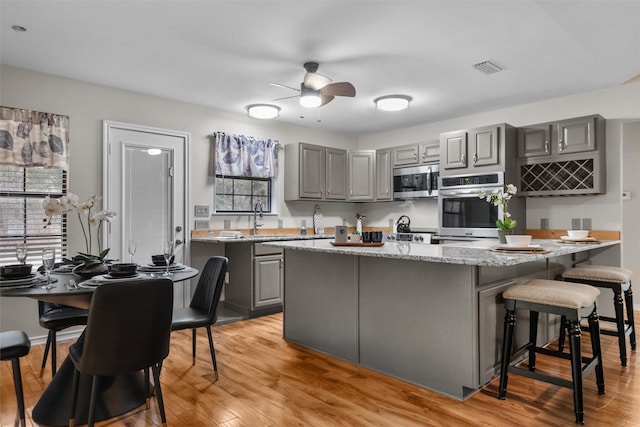 kitchen with a center island, stainless steel appliances, gray cabinetry, light wood-type flooring, and a kitchen breakfast bar