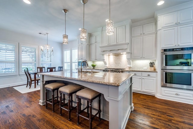 kitchen featuring stainless steel double oven, under cabinet range hood, stove, a sink, and backsplash