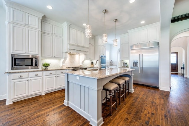 kitchen with arched walkways, white cabinetry, under cabinet range hood, and built in appliances