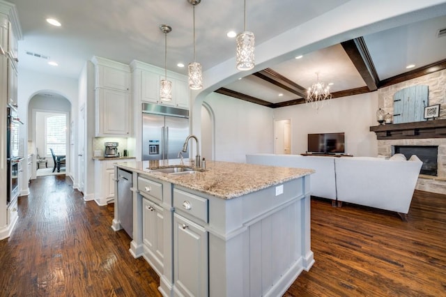 kitchen with arched walkways, stainless steel appliances, a sink, white cabinetry, and dark wood finished floors