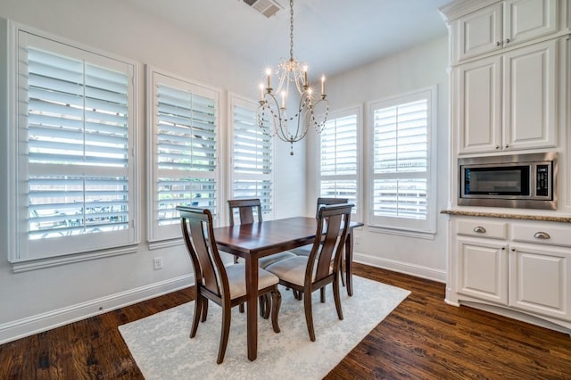 dining area featuring dark wood-style flooring, visible vents, a notable chandelier, and baseboards