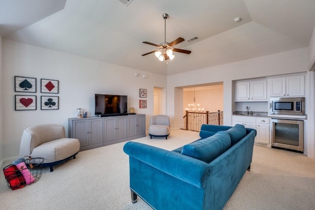 living area featuring wine cooler, a tray ceiling, visible vents, light carpet, and ceiling fan with notable chandelier