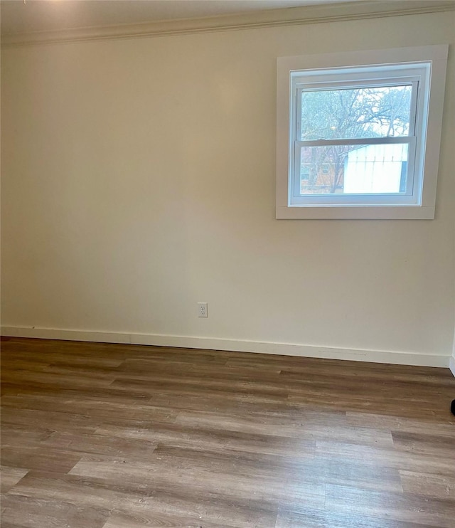 spare room with baseboards, wood finished floors, and crown molding