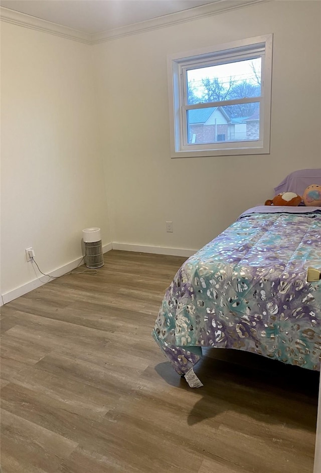 bedroom featuring baseboards, wood finished floors, and crown molding