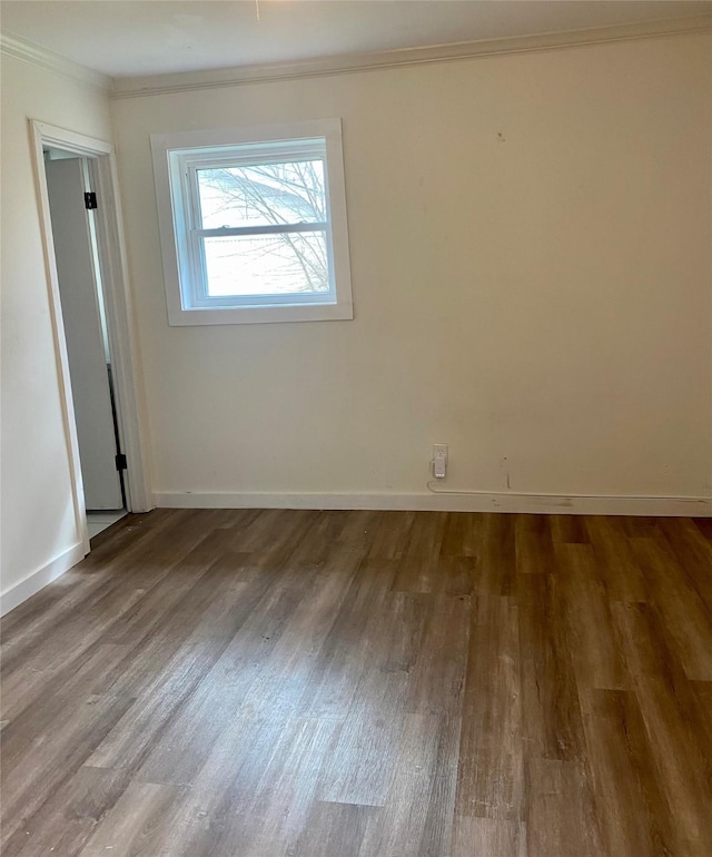 empty room featuring baseboards, crown molding, and wood finished floors