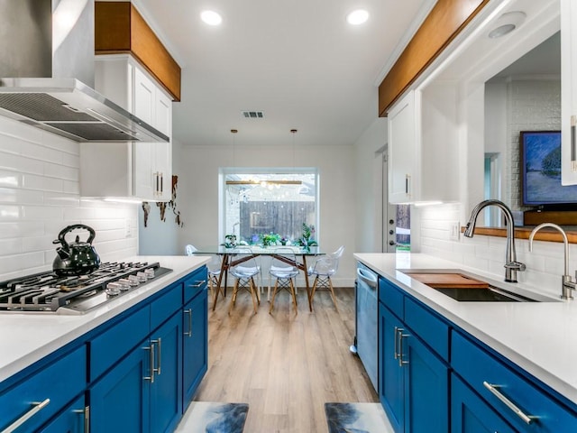 kitchen featuring light wood-style flooring, a sink, blue cabinets, appliances with stainless steel finishes, and wall chimney exhaust hood