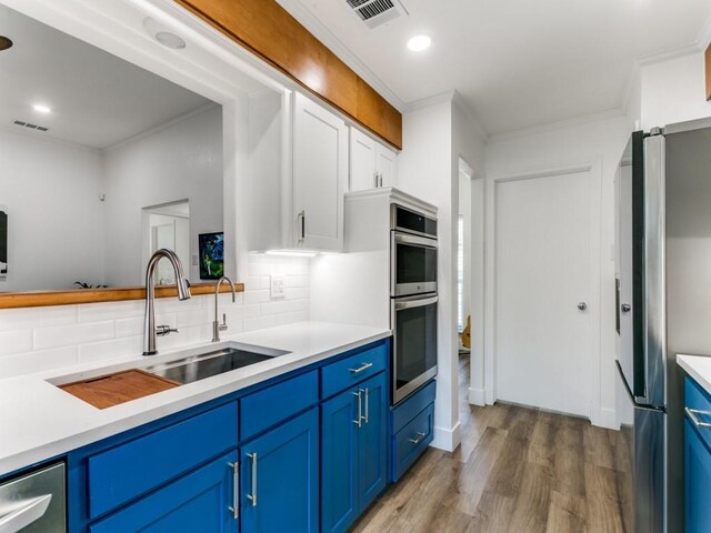 kitchen with a sink, blue cabinetry, light wood finished floors, and stainless steel appliances