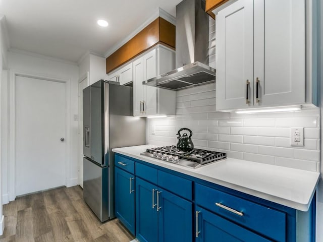 kitchen with dark wood-type flooring, light countertops, appliances with stainless steel finishes, wall chimney range hood, and blue cabinets