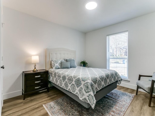 bedroom with multiple windows, wood finished floors, and baseboards