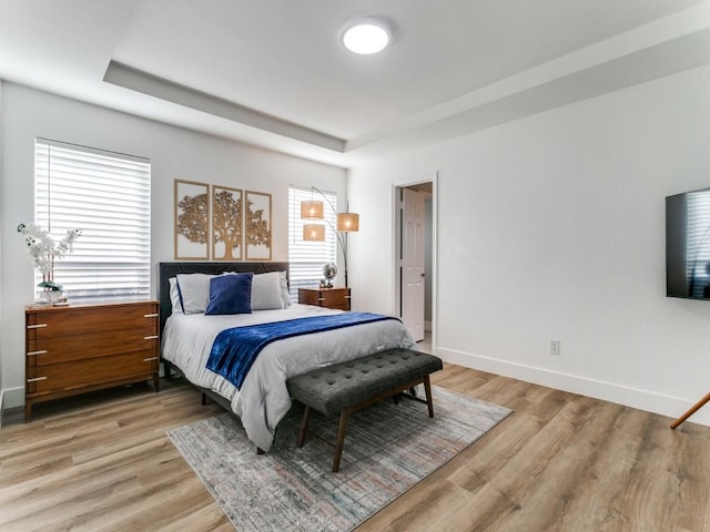 bedroom featuring baseboards, a raised ceiling, and light wood finished floors