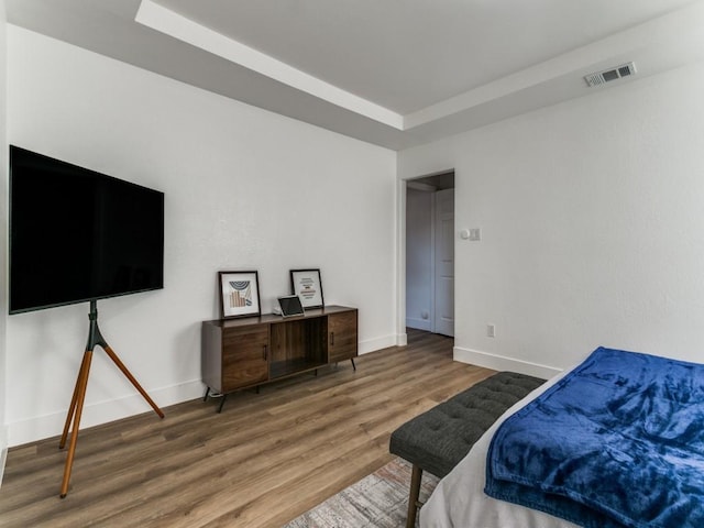 bedroom featuring visible vents, a raised ceiling, baseboards, and wood finished floors