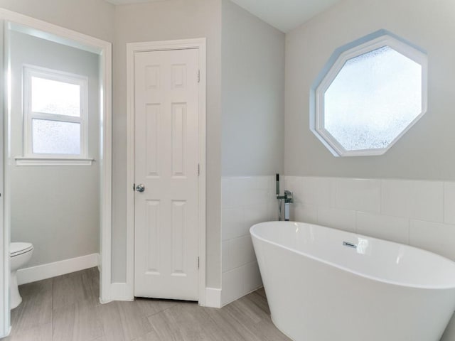 full bathroom featuring a soaking tub, toilet, and tile walls