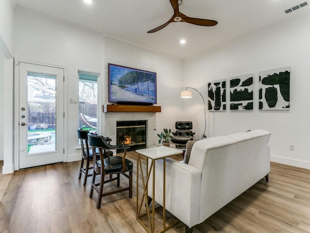 living room with visible vents, a ceiling fan, wood finished floors, baseboards, and a brick fireplace