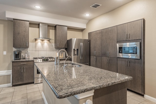 kitchen featuring stainless steel appliances, a sink, visible vents, dark brown cabinets, and wall chimney range hood