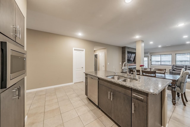 kitchen featuring light stone counters, a kitchen island with sink, stainless steel appliances, a sink, and open floor plan