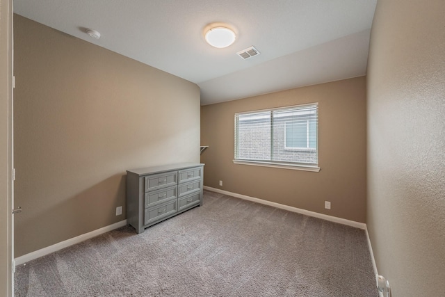 unfurnished bedroom with baseboards, lofted ceiling, visible vents, and light colored carpet