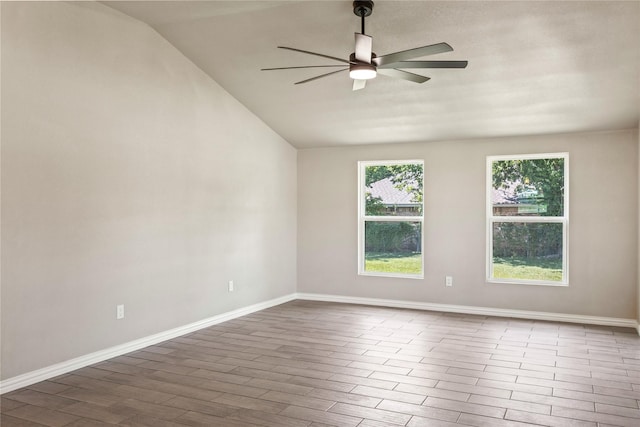 empty room with a ceiling fan, vaulted ceiling, baseboards, and wood finished floors