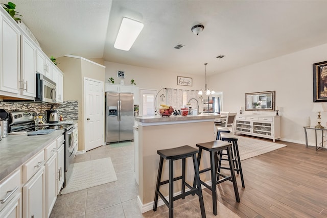 kitchen with a center island with sink, stainless steel appliances, light countertops, decorative backsplash, and white cabinets