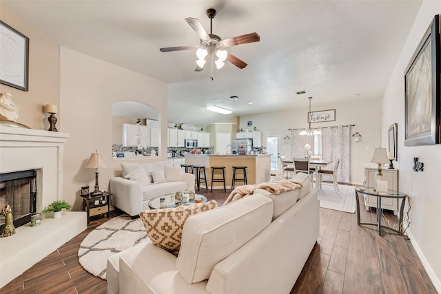 living area with a ceiling fan, a fireplace with raised hearth, dark wood finished floors, and baseboards