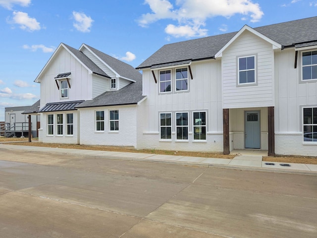 modern farmhouse with a standing seam roof, roof with shingles, brick siding, and board and batten siding