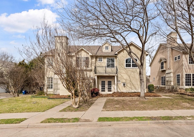 view of front of property with a front yard, a balcony, a shingled roof, stucco siding, and french doors