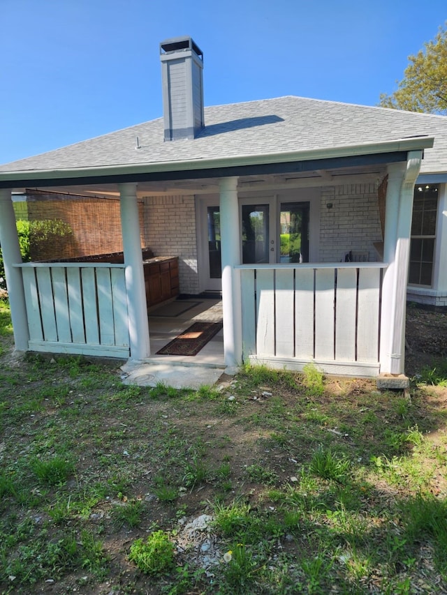 rear view of property with roof with shingles, brick siding, and a chimney