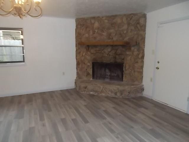 unfurnished living room with a notable chandelier, a fireplace, and wood finished floors