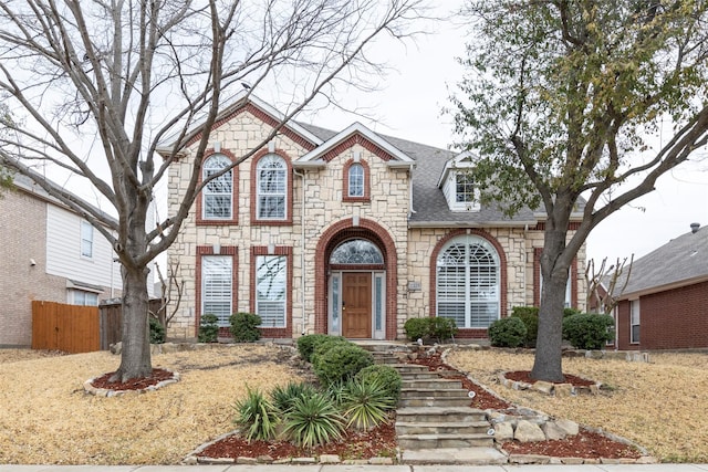 view of front of home with stone siding, roof with shingles, and fence